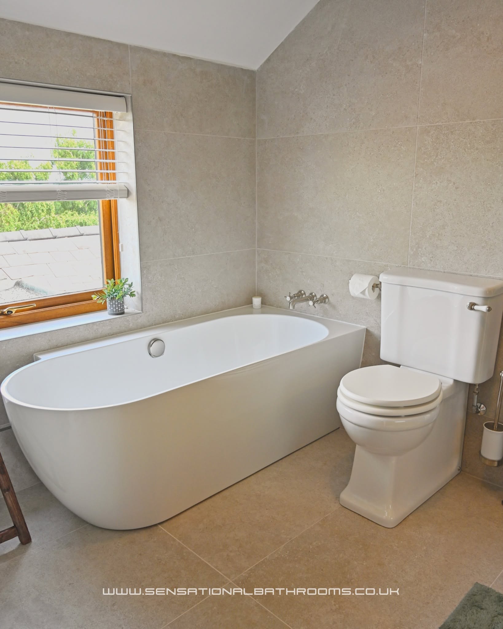 Modern freestanding bathtub in a renovated bathroom with stone-look tiles and natural window light