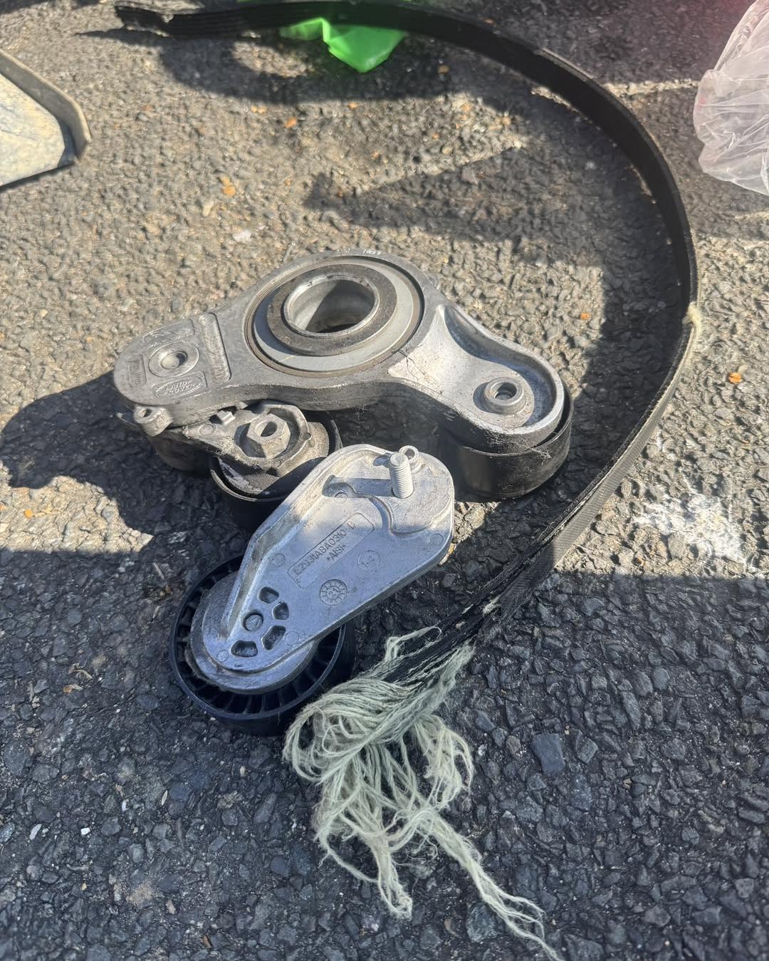 Removed drive belt and tensioner assembly laid out on the ground