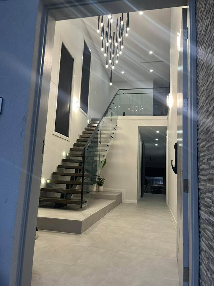 Double-height entry with a floating staircase, glass balustrade and pendant lighting