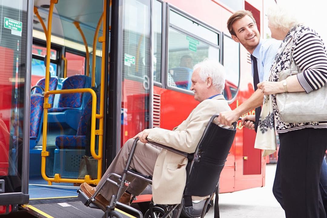 Support worker helping a wheelchair user board an accessible bus with a ramp
