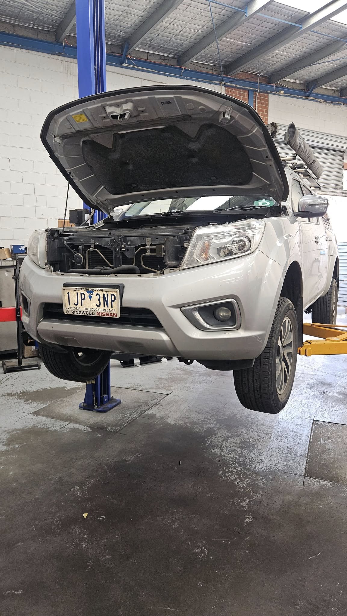 Silver Nissan Navara 4WD on a hoist with bonnet open during a service