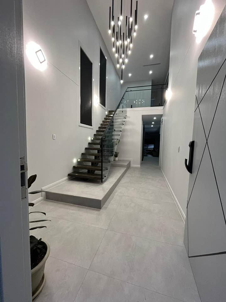 Double-height entry with a floating timber staircase, glass balustrade and black pendant lights