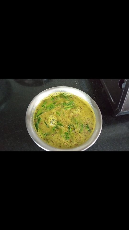 A bowl of freshly prepared green rasam with curry leaves