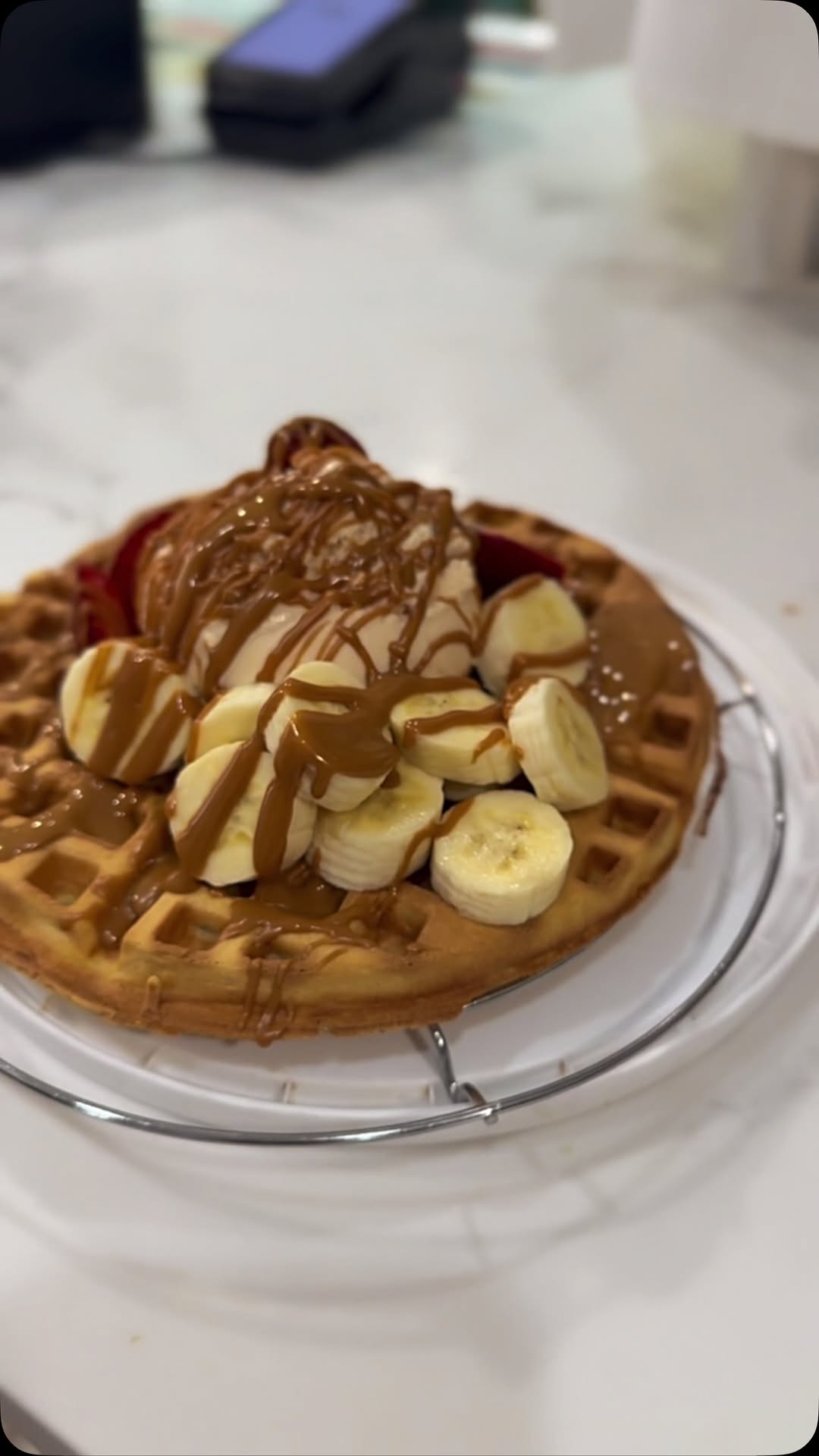Waffle with ice cream, banana slices and caramel drizzle on a wire rack