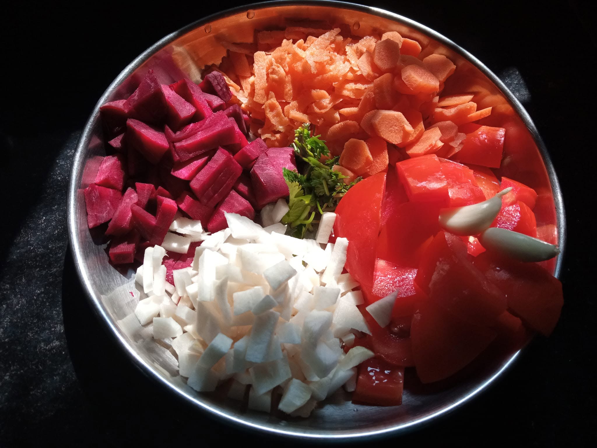 Fresh colourful vegetables — beetroot, carrots, tomato and onion — in a steel bowl ready for cooking