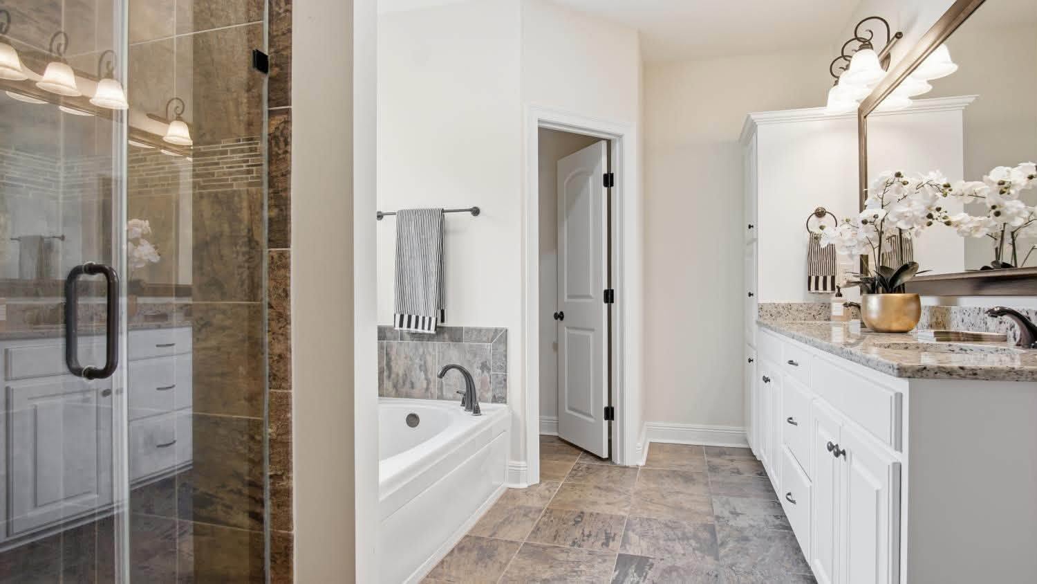 A bathroom with a built-in bathtub, glass shower screen and granite vanity