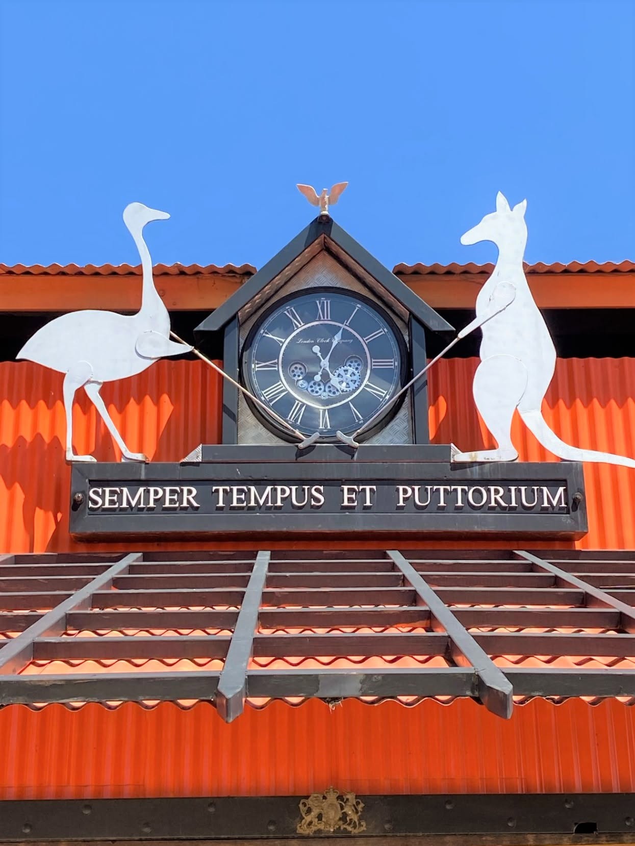 Outback Opal Putters entrance — steampunk clock tower with metal emu and kangaroo sculptures on orange corrugated iron building, Lightning Ridge NSW