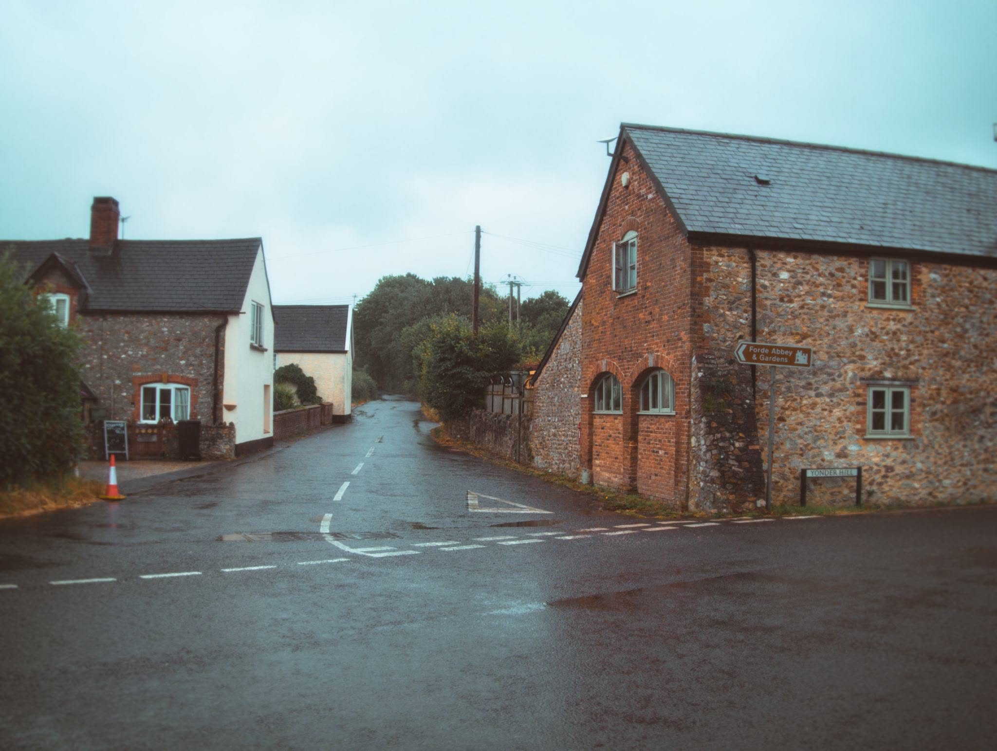 Colour photograph of a wet English village road with historic stone and brick buildings