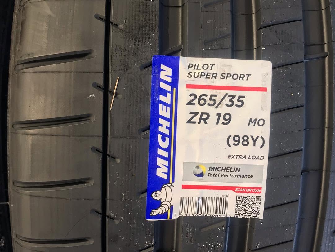 Four Michelin Pilot Sport tyres lined up in front of a black Mercedes-AMG at the workshop