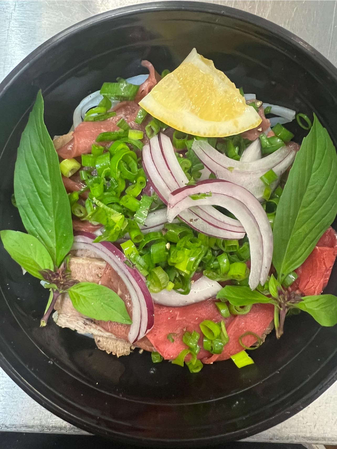 Close-up of a Cheryl-Lyn's beef pho bowl with thinly sliced beef, red onion, spring onion and Thai basil
