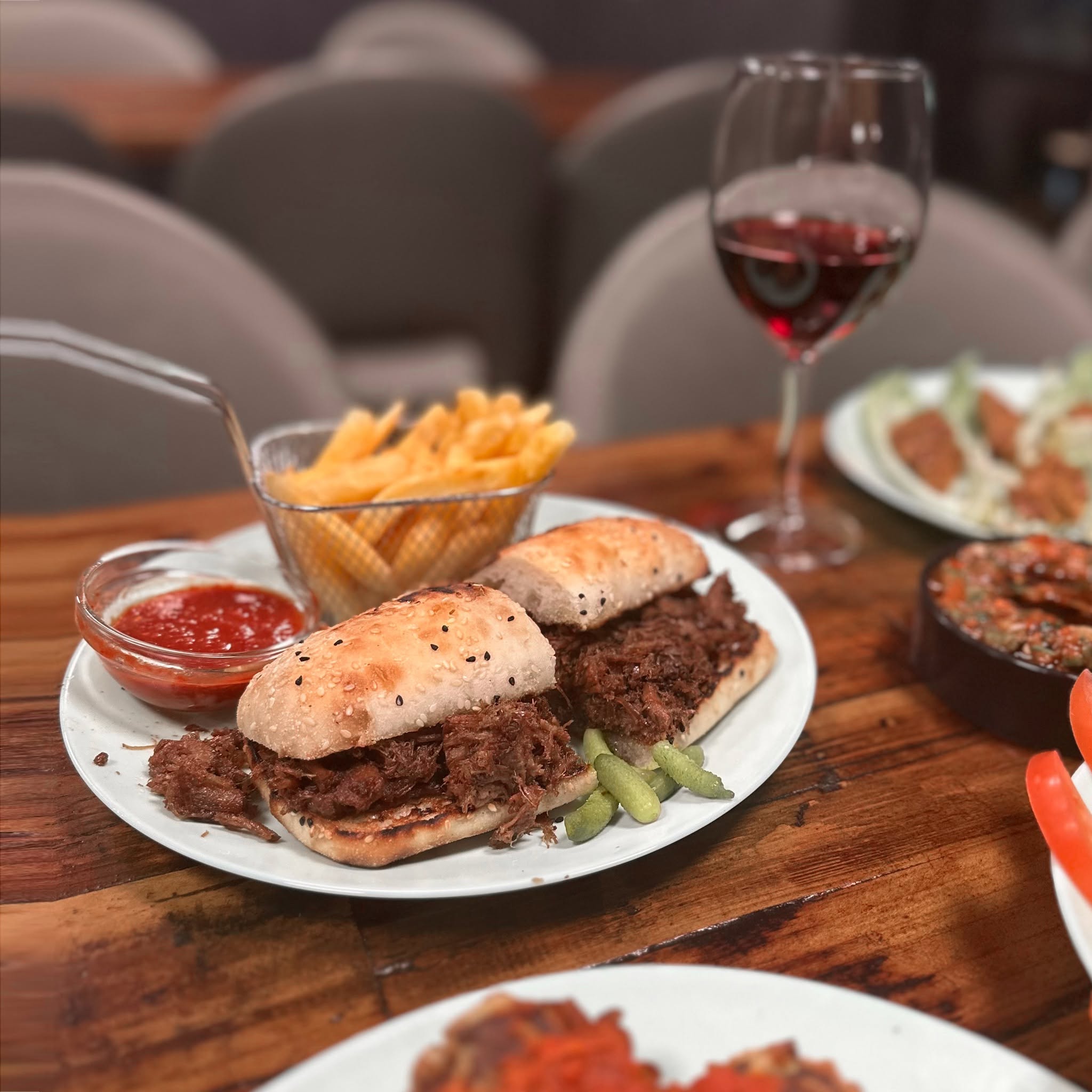 Slow-cooked meat sandwich with chips, sauce and a glass of red wine