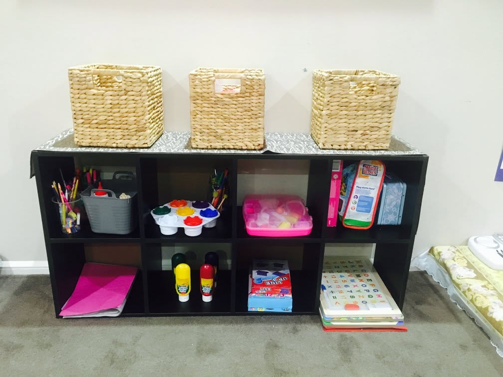Well-stocked art and activity shelf at Orchard Family Day Care with paints, craft supplies, and educational toys