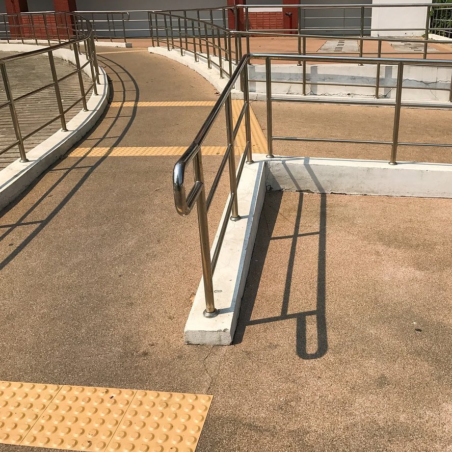 Person with a white cane standing at a tactile ground surface indicator at a pedestrian crossing