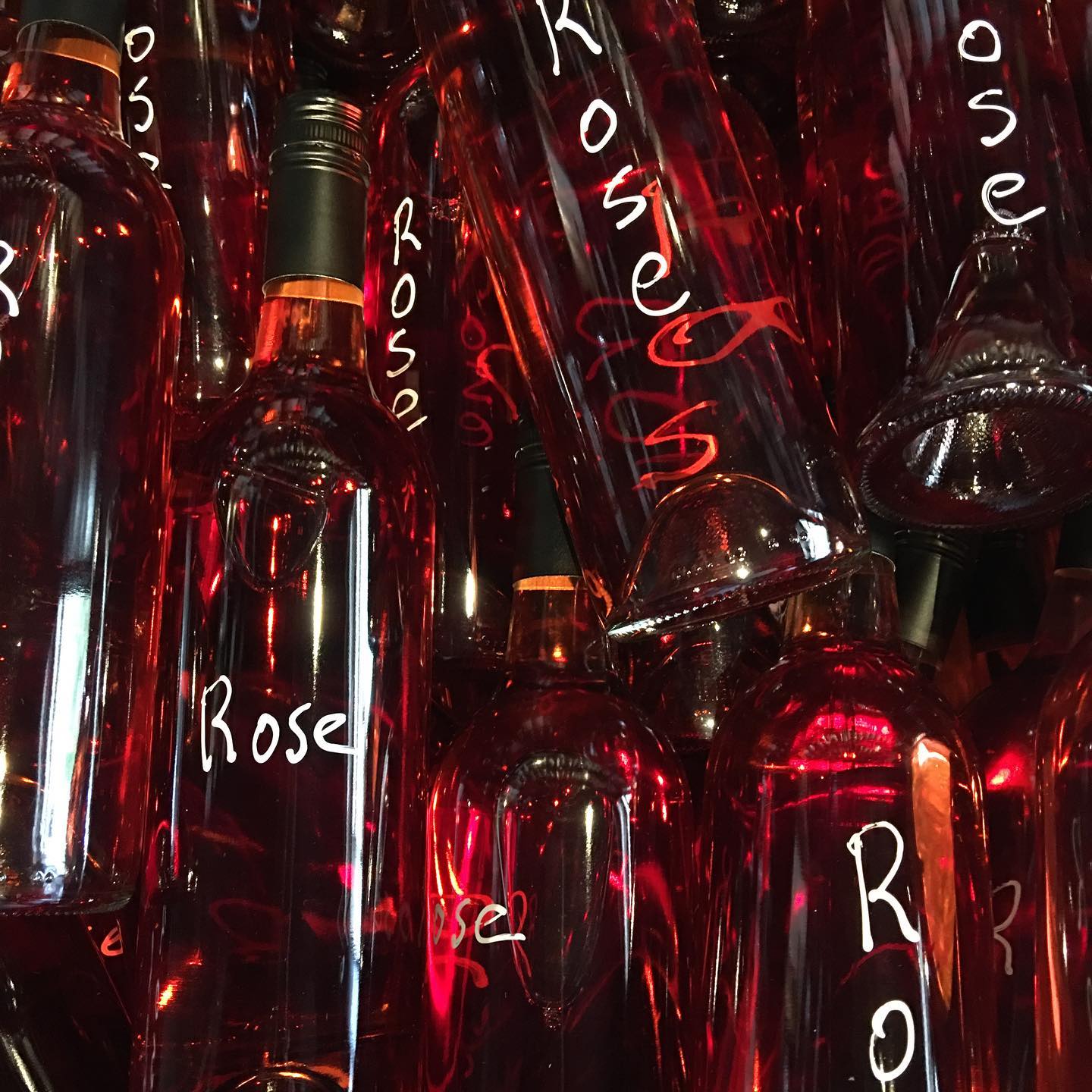 Stacked clear bottles of rosé wine with the word Rose handwritten in white pen