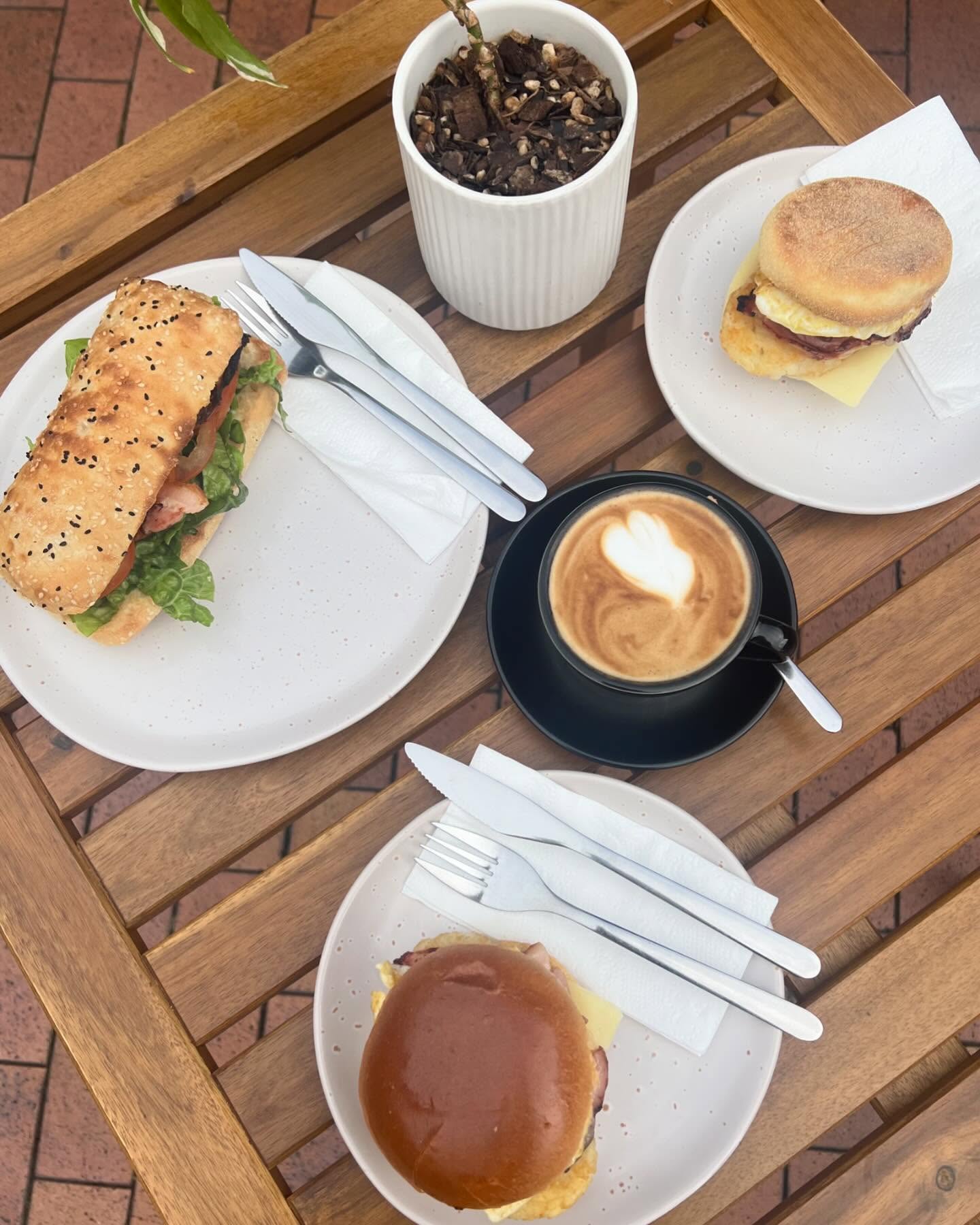 Hygge Cafe breakfast spread — baguette rolls, egg muffins and latte on a timber outdoor table