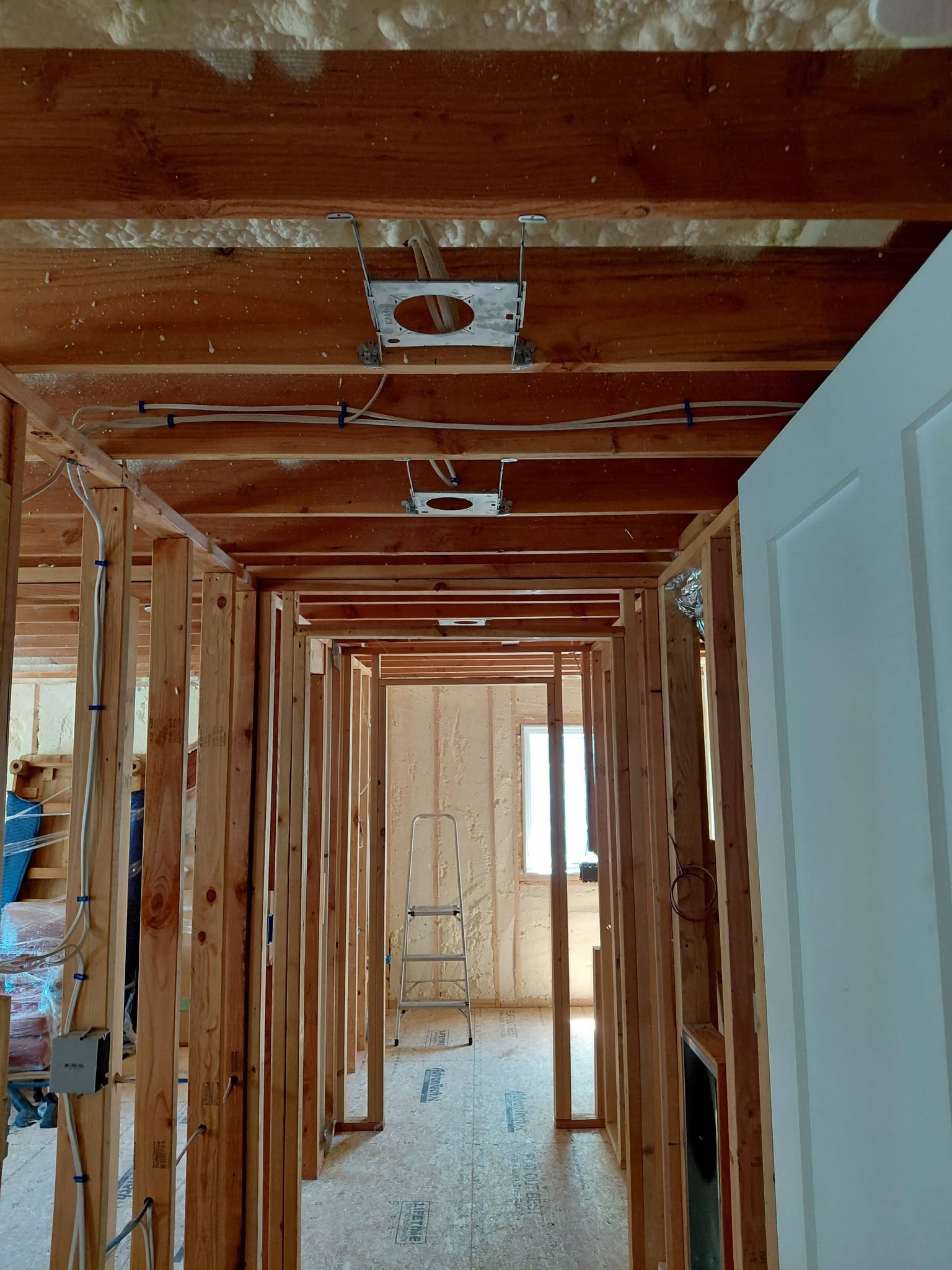 Electrical rough-in work showing wiring and recessed light installation in a framed hallway ceiling