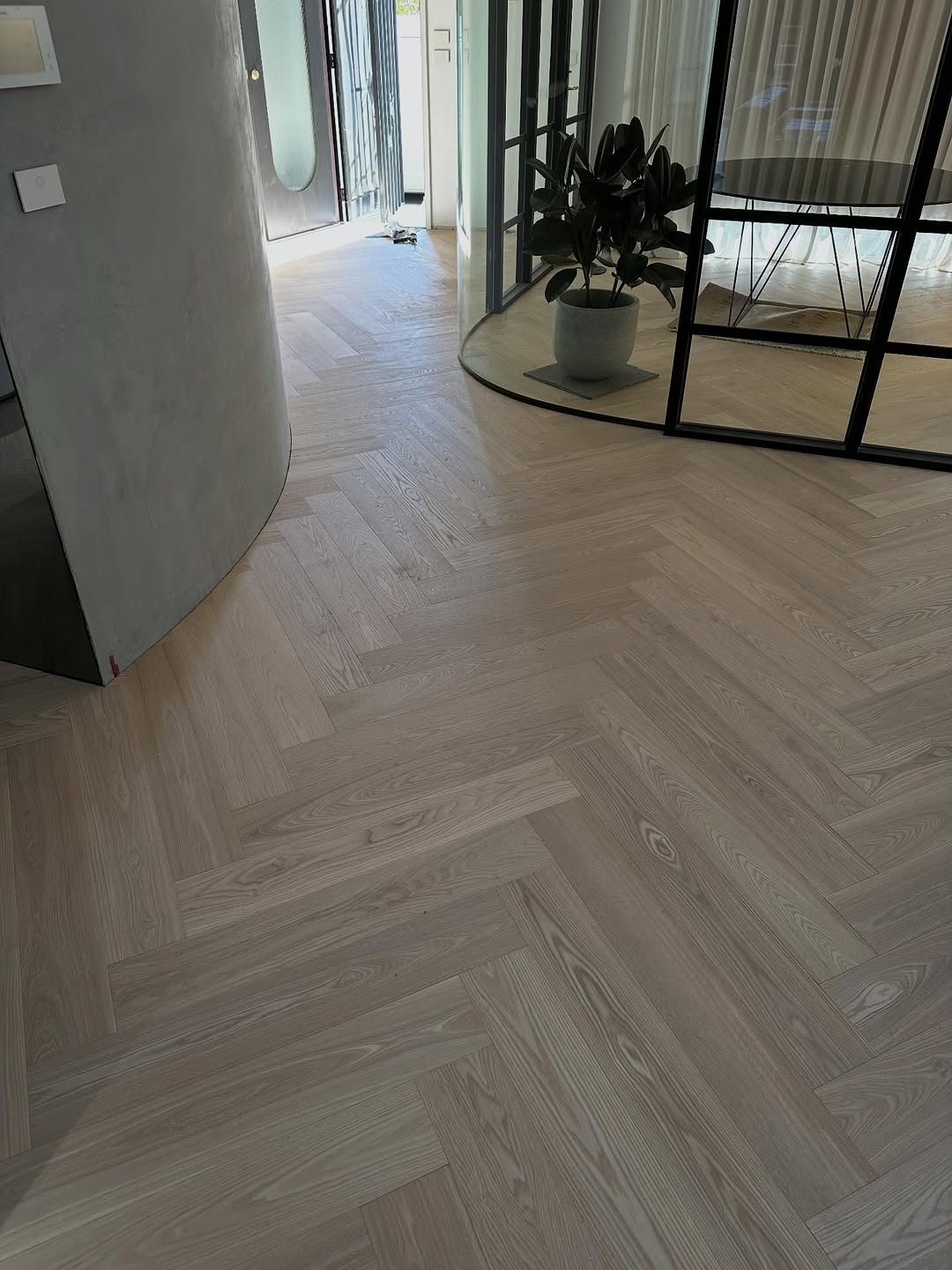 Light herringbone timber floor pattern in a modern entry with curved concrete wall and glass partition