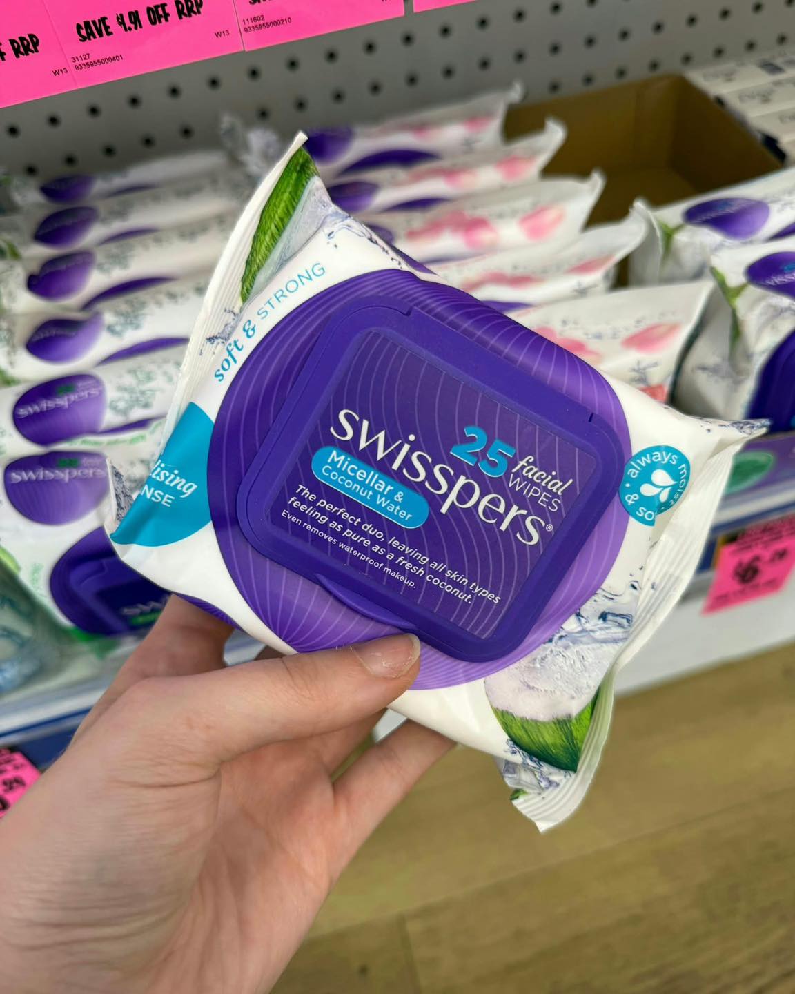 Pack of Swisspers facial wipes held in front of a shelf of wipes
