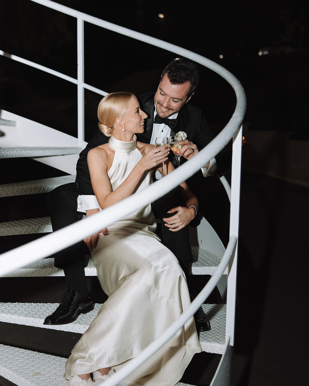 Wedding couple toasting champagne on a spiral staircase with white railings at a night reception