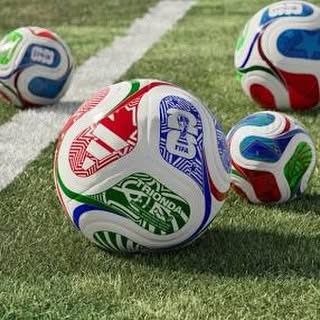 Colourful footballs resting on a grass pitch beside a white line