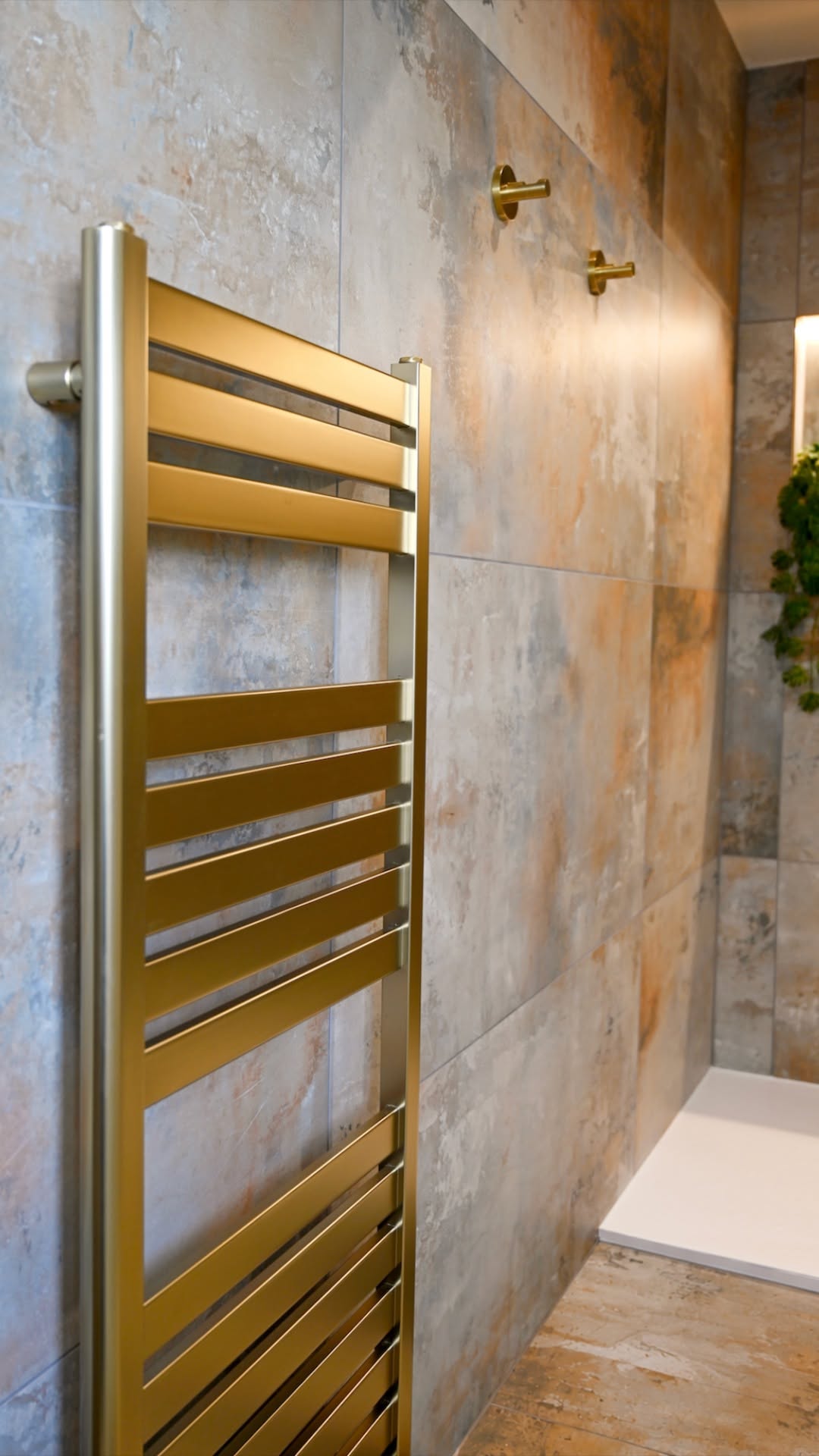 Brushed gold towel rail against textured rust-tone stone-look tiled bathroom wall