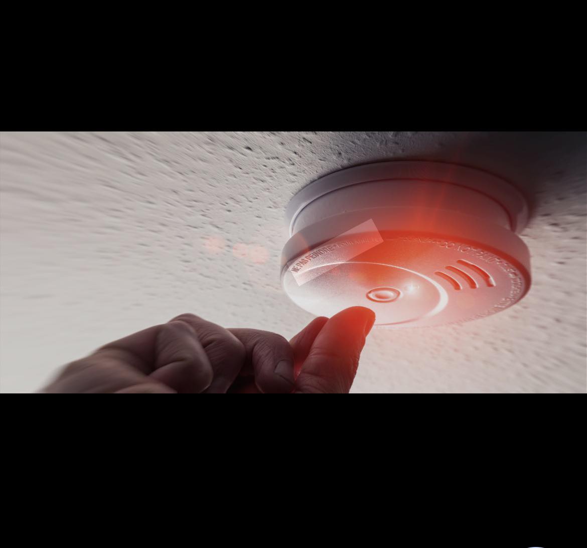 Smoke alarm being tested — red light glowing on ceiling-mounted detector