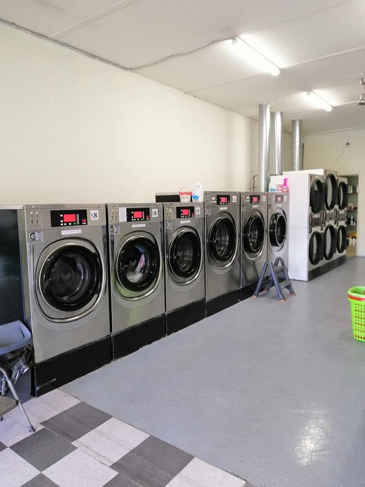 Row of stainless steel self-service washing machines and stacked dryers inside Chandler Coin Laundry