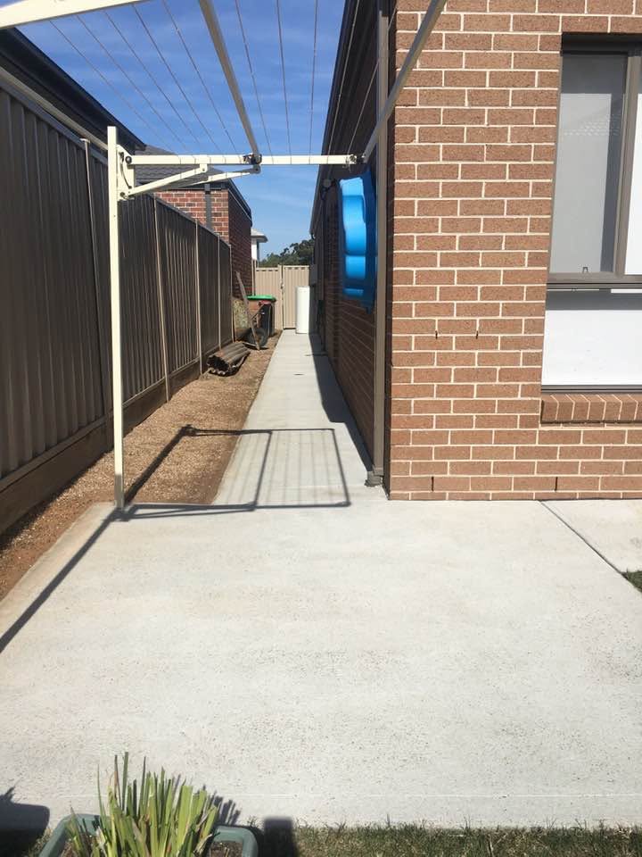 Freshly pressure cleaned concrete walkway alongside a brick house on a clear day