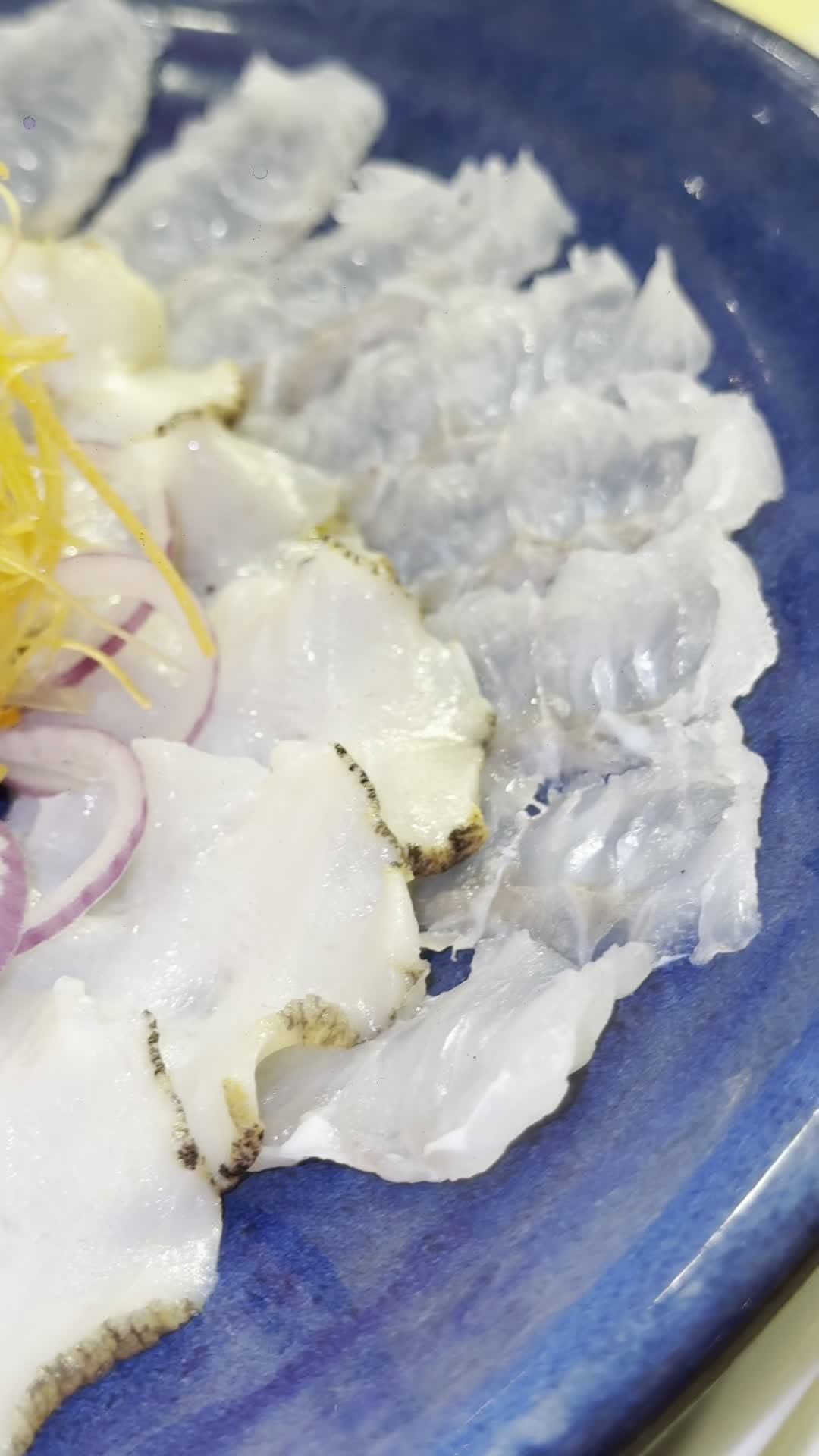 A plate of fresh raw fish slices on a blue ceramic dish