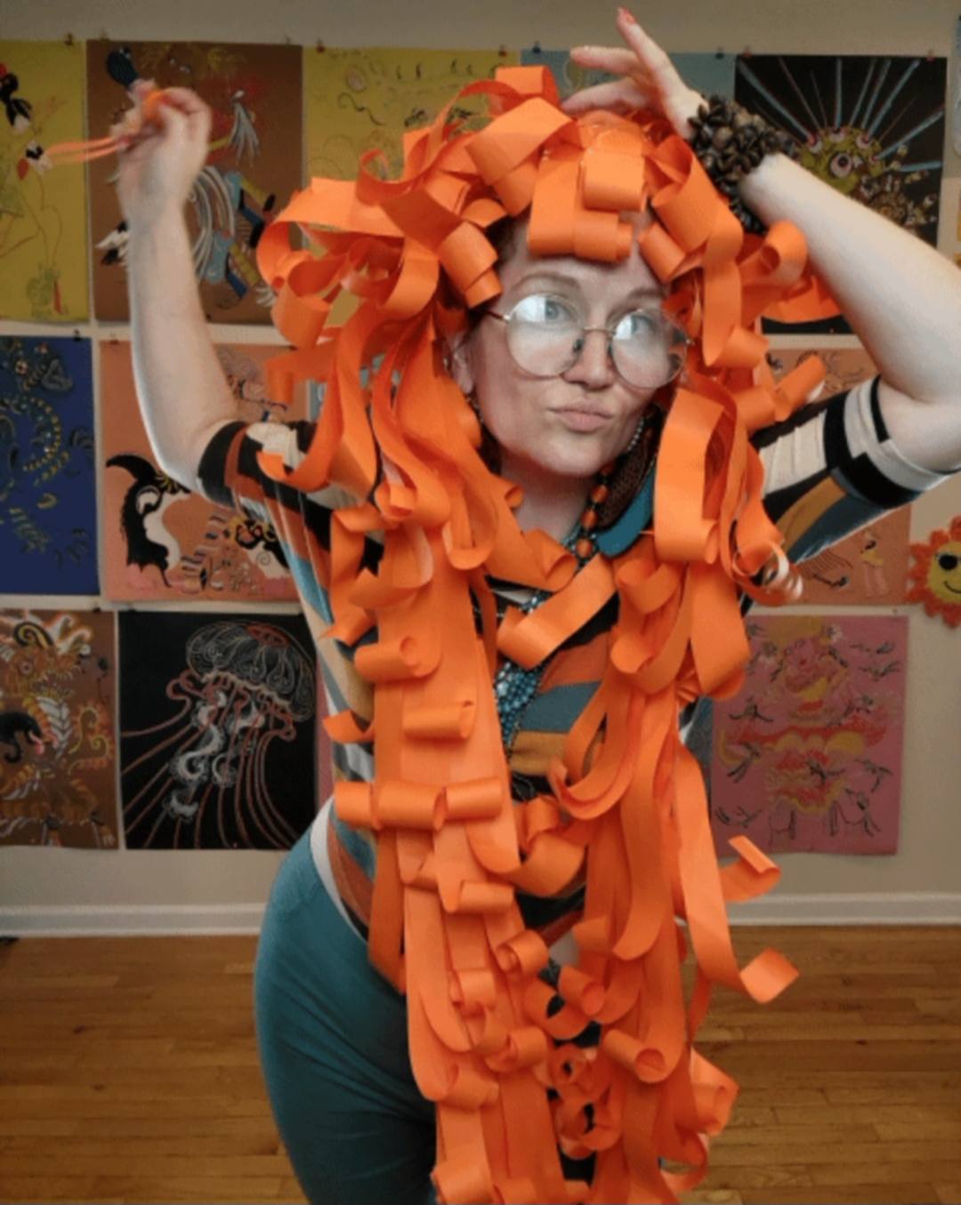 Donna wearing a dramatic orange cascading paper wig in her art studio
