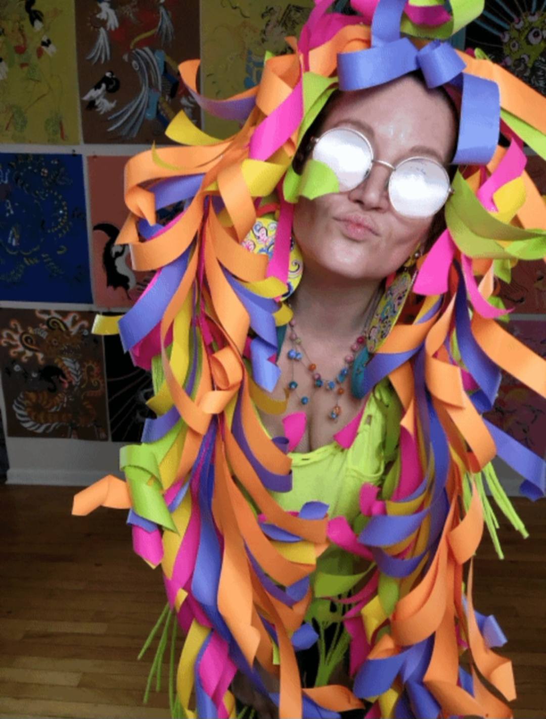 Donna Marie Milligan wearing a neon paper wig made from cascading green, orange, pink, purple, and yellow strips.