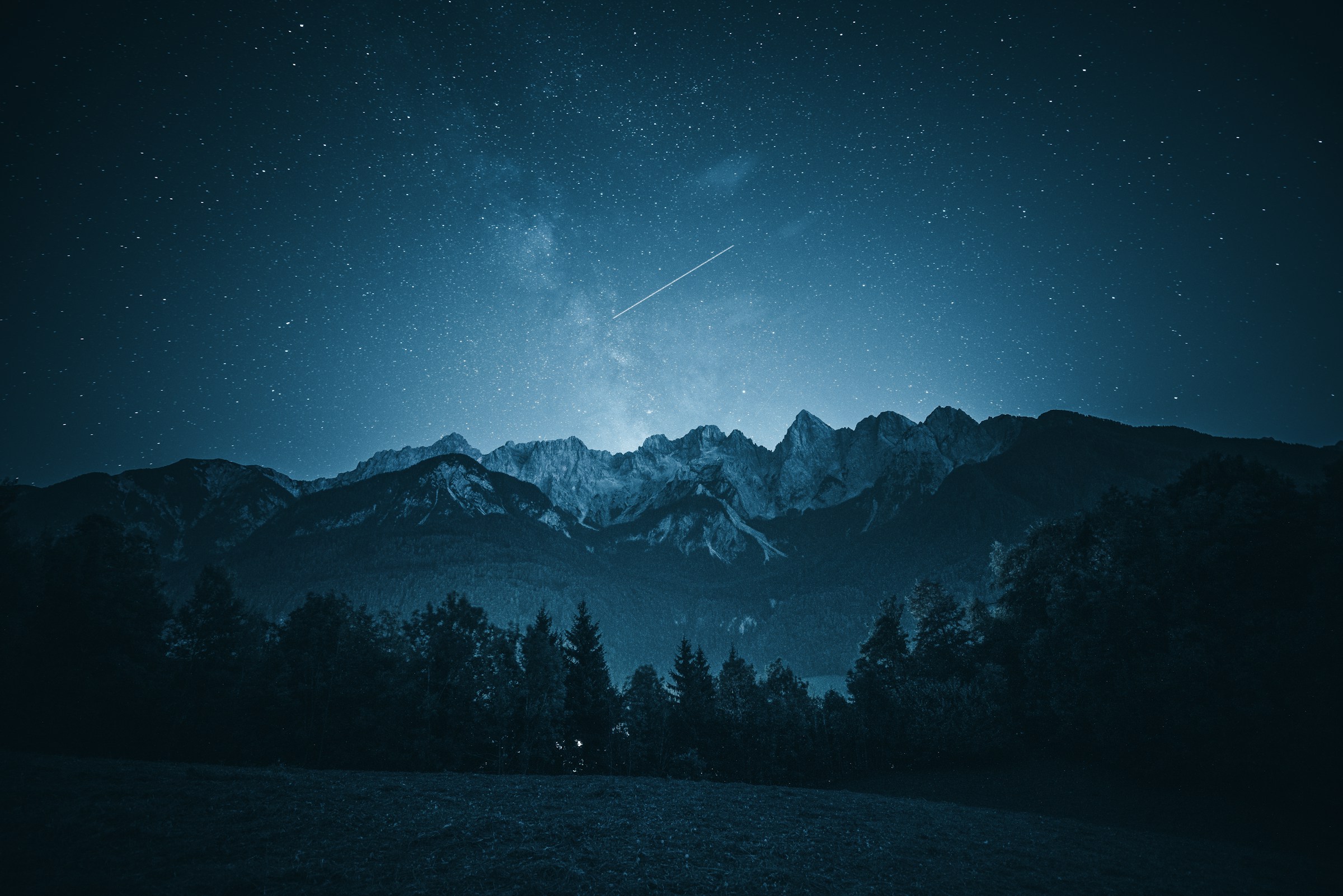 Night sky with Milky Way over mountain range with shooting star