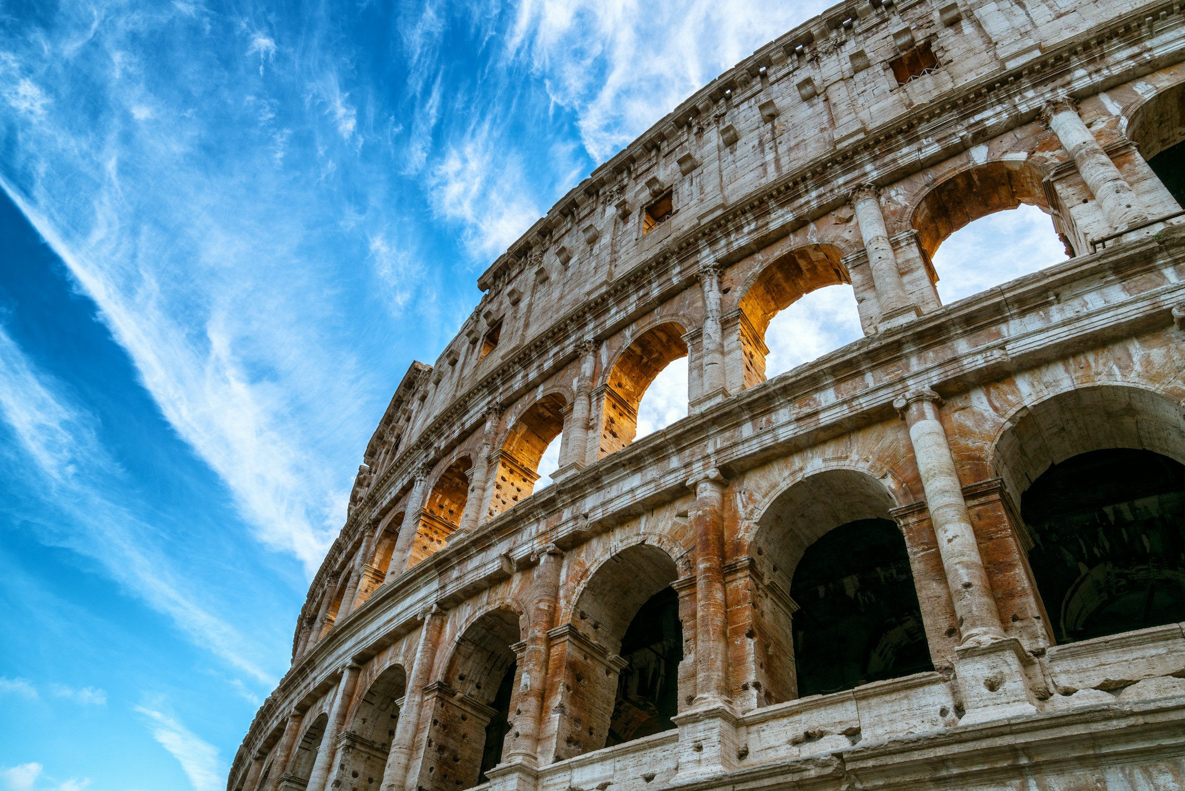 Roman Colosseum architecture against blue sky with wispy clouds