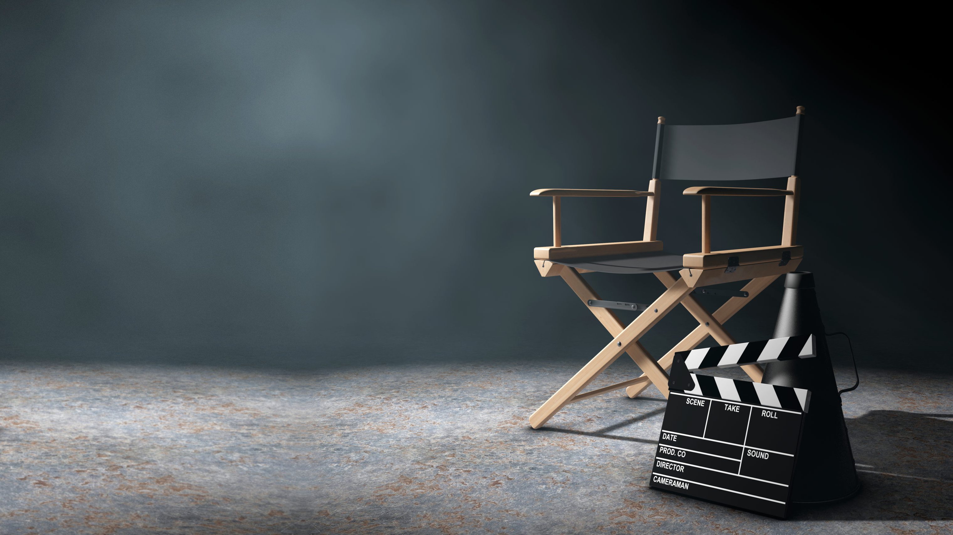 An empty director's chair, clapperboard and megaphone on a dark soundstage