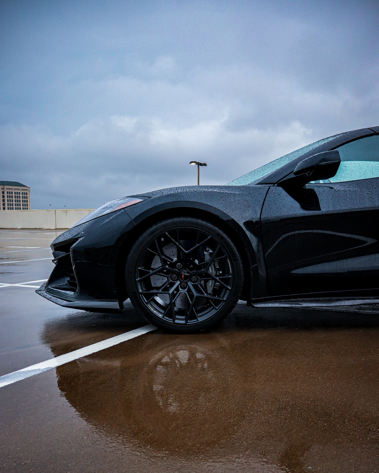 Black C8 Corvette side profile on wet rooftop parking lot with moody sky