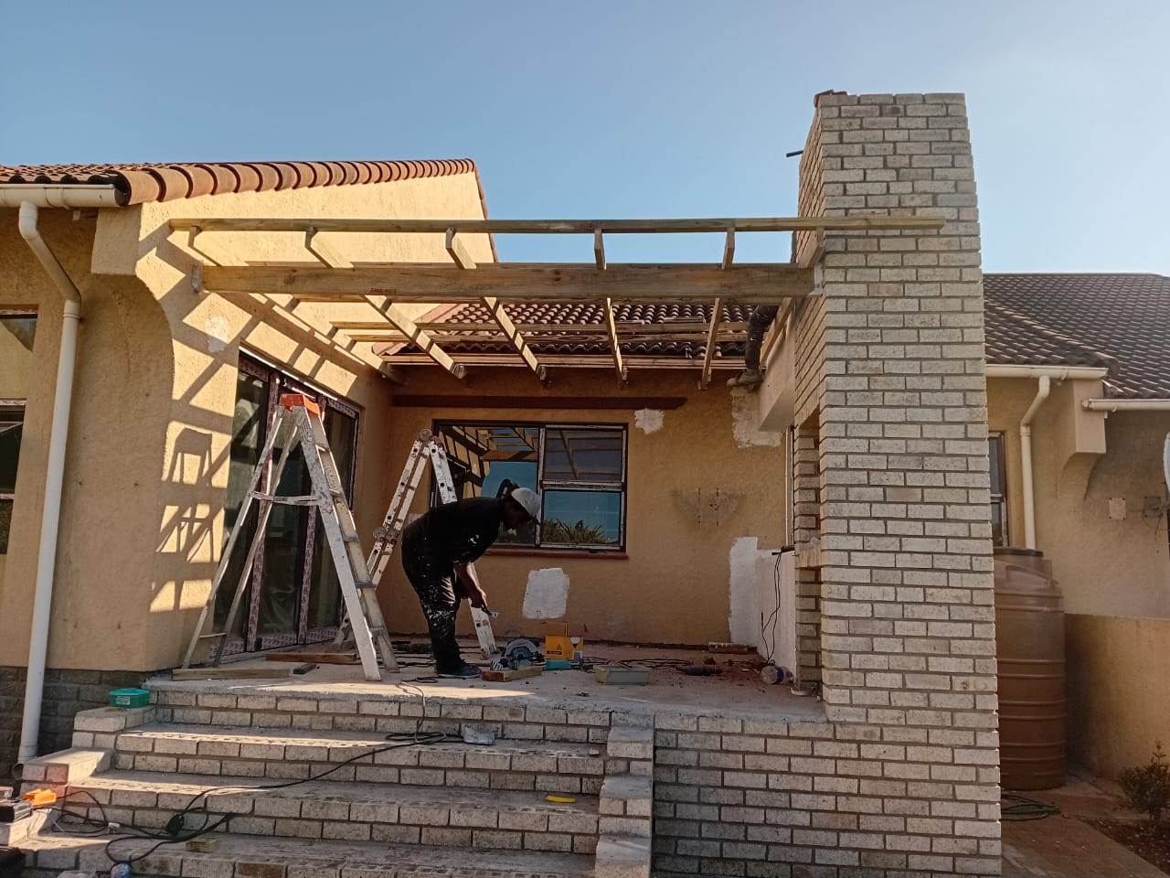 Patio roof construction Gqeberha — wooden beams and metal roof frame with brick columns, work in progress