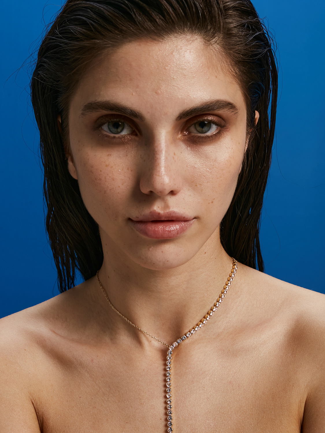 Beauty editorial before retouching — natural freckled skin on blue background