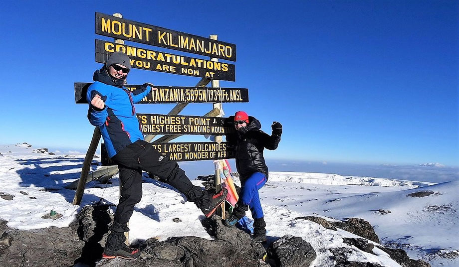 Climbers celebrating at the Mount Kilimanjaro summit sign