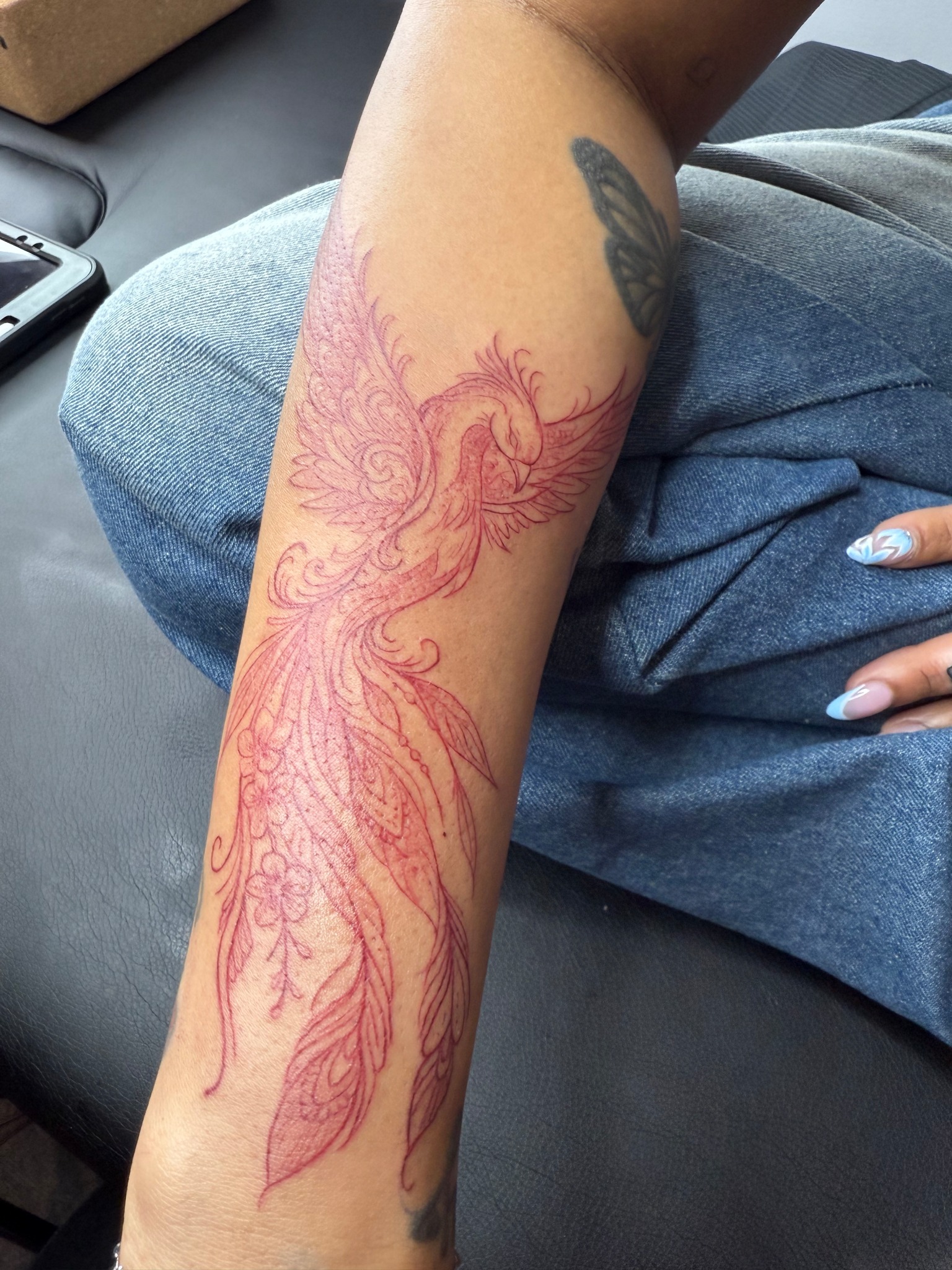 Red line-work phoenix tattoo on a forearm with cherry blossoms