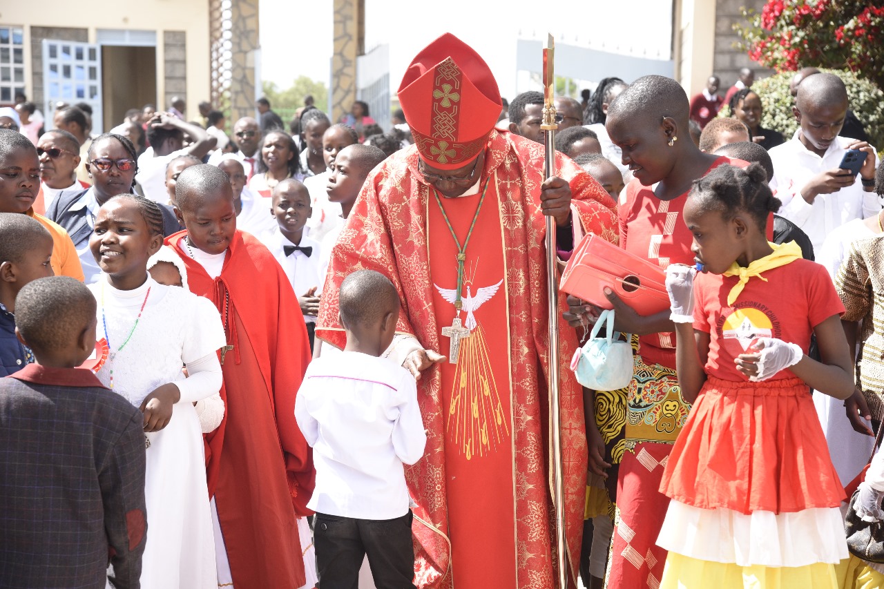 Bishop in red vestments blessing and interacting with children after Mass