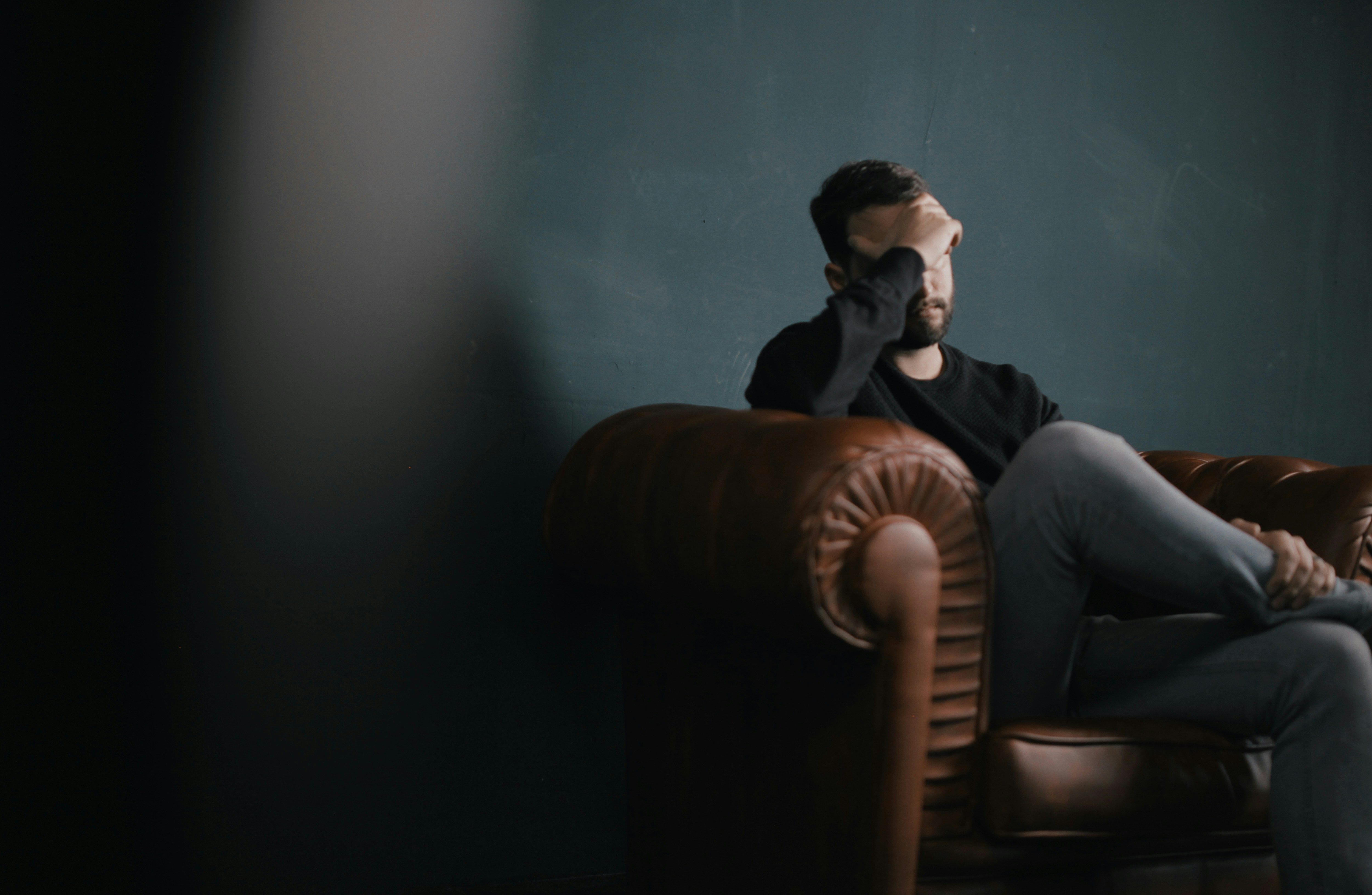 Person sitting in dim room covering face, illustrating mental health challenges