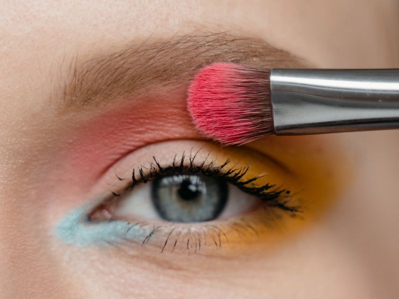 Close-up of an eye with colorful eyeshadow being applied with a makeup brush.