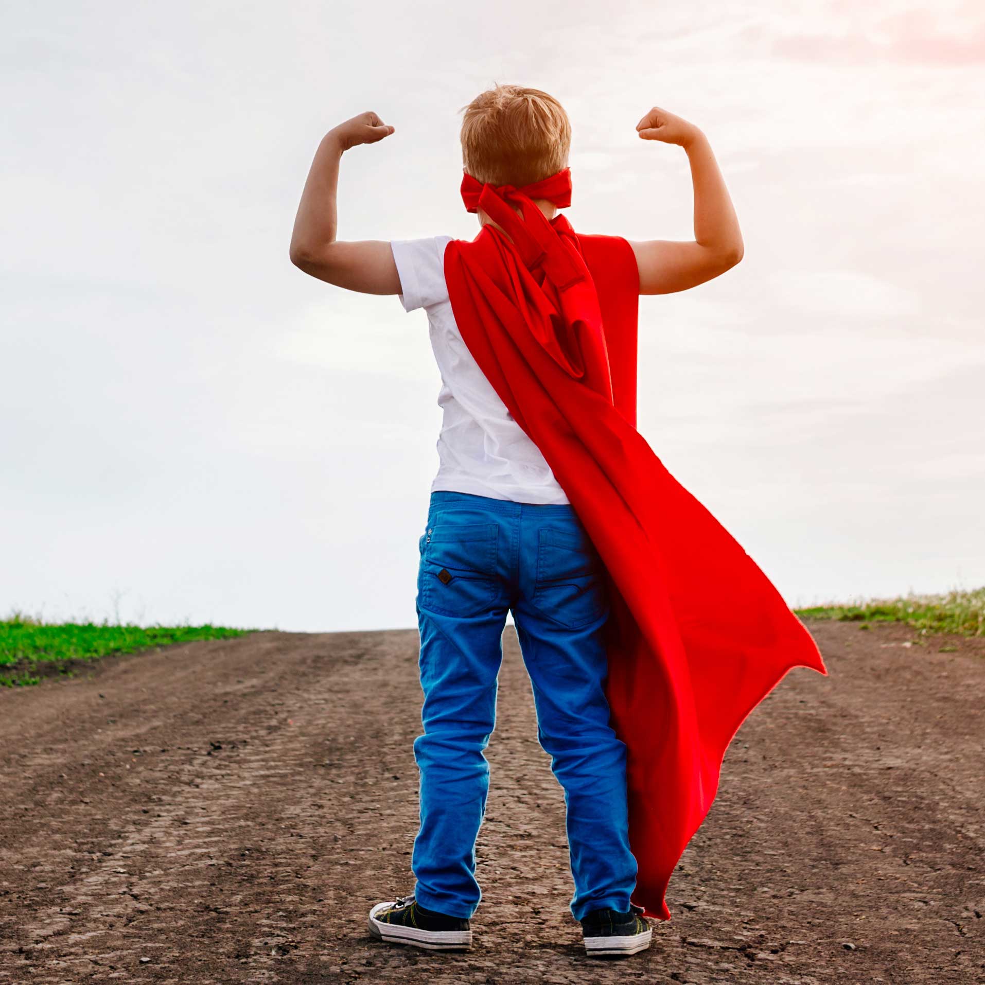 Hero image of a child in a red superhero cape flexing muscles on a dirt road