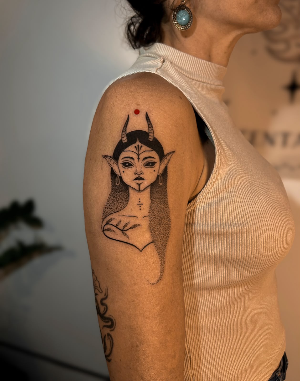 Ombro com criatura élfica com chifres e ponto vermelho, regata branca