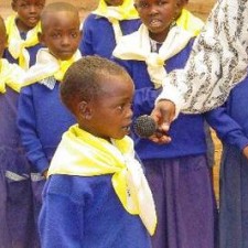 Kind in blauer Schuluniform spricht mit Mikrofon bei einer Schulveranstaltung