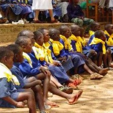 Reihe von Schulkindern in blauen Uniformen sitzen barfuß bei einer Schulveranstaltung