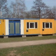 Drei aufgestellte gelb-blaue Container auf der Wiese im Frühling