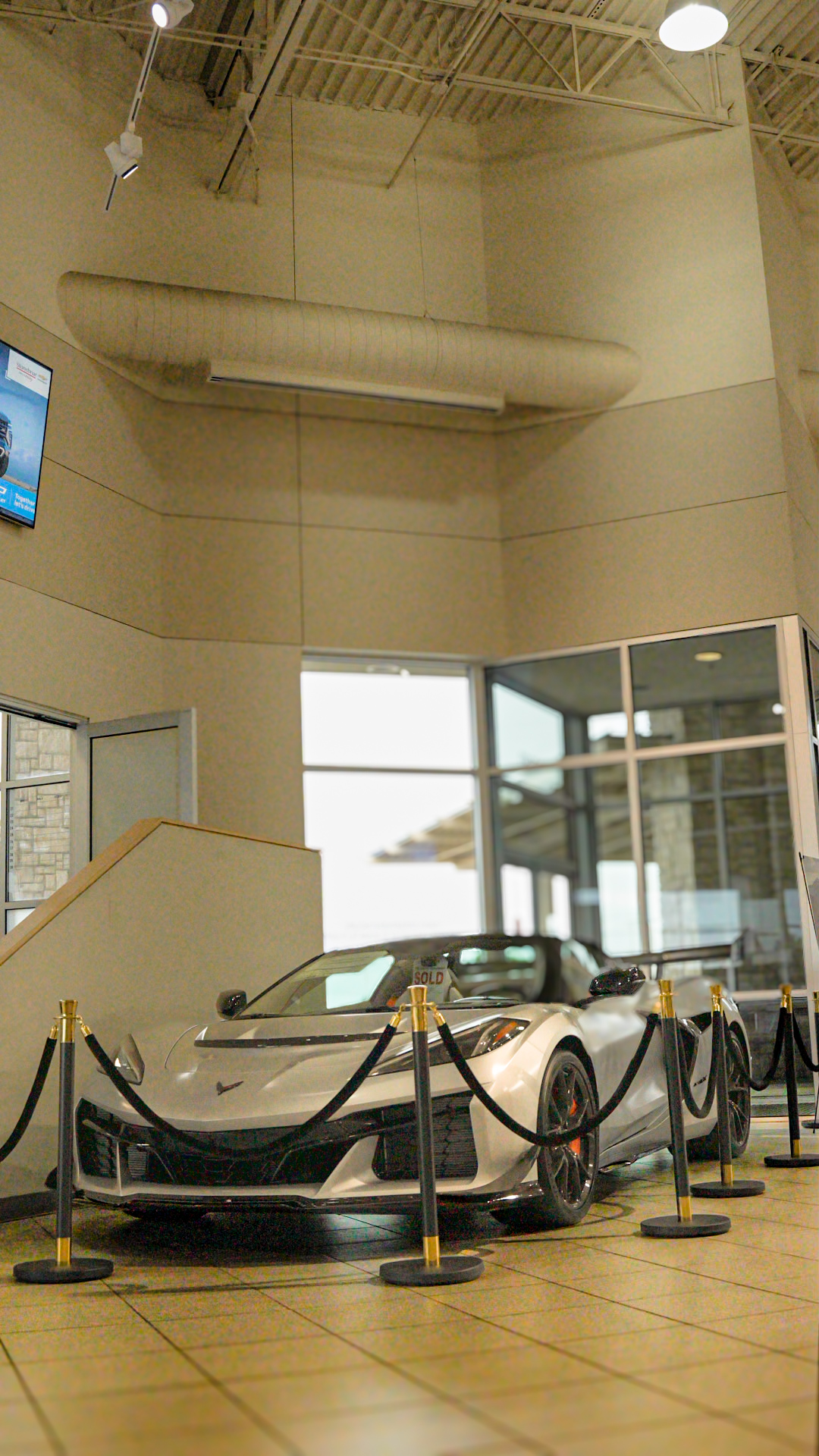 Silver C8 Corvette displayed in dealership showroom with velvet rope barriers