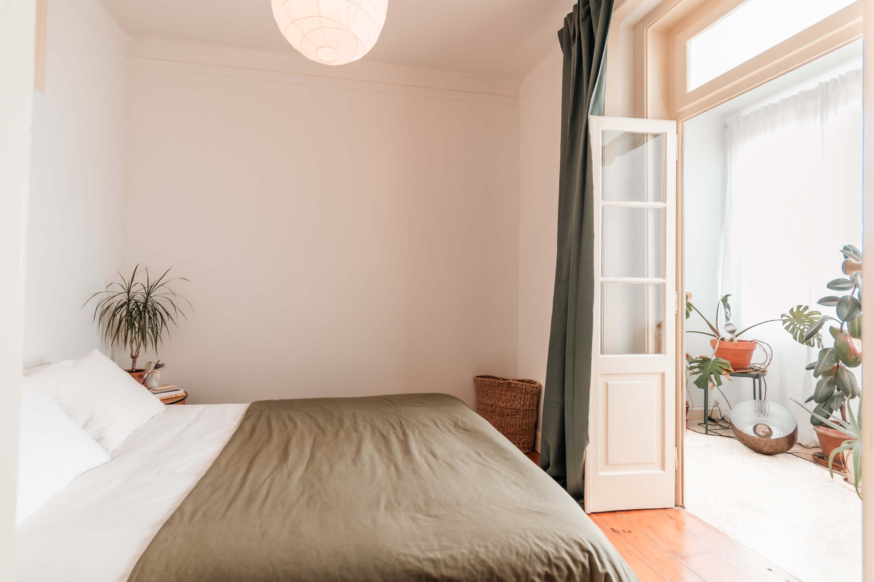 Serene bedroom with olive green bedding, indoor plants, and traditional Portuguese windows