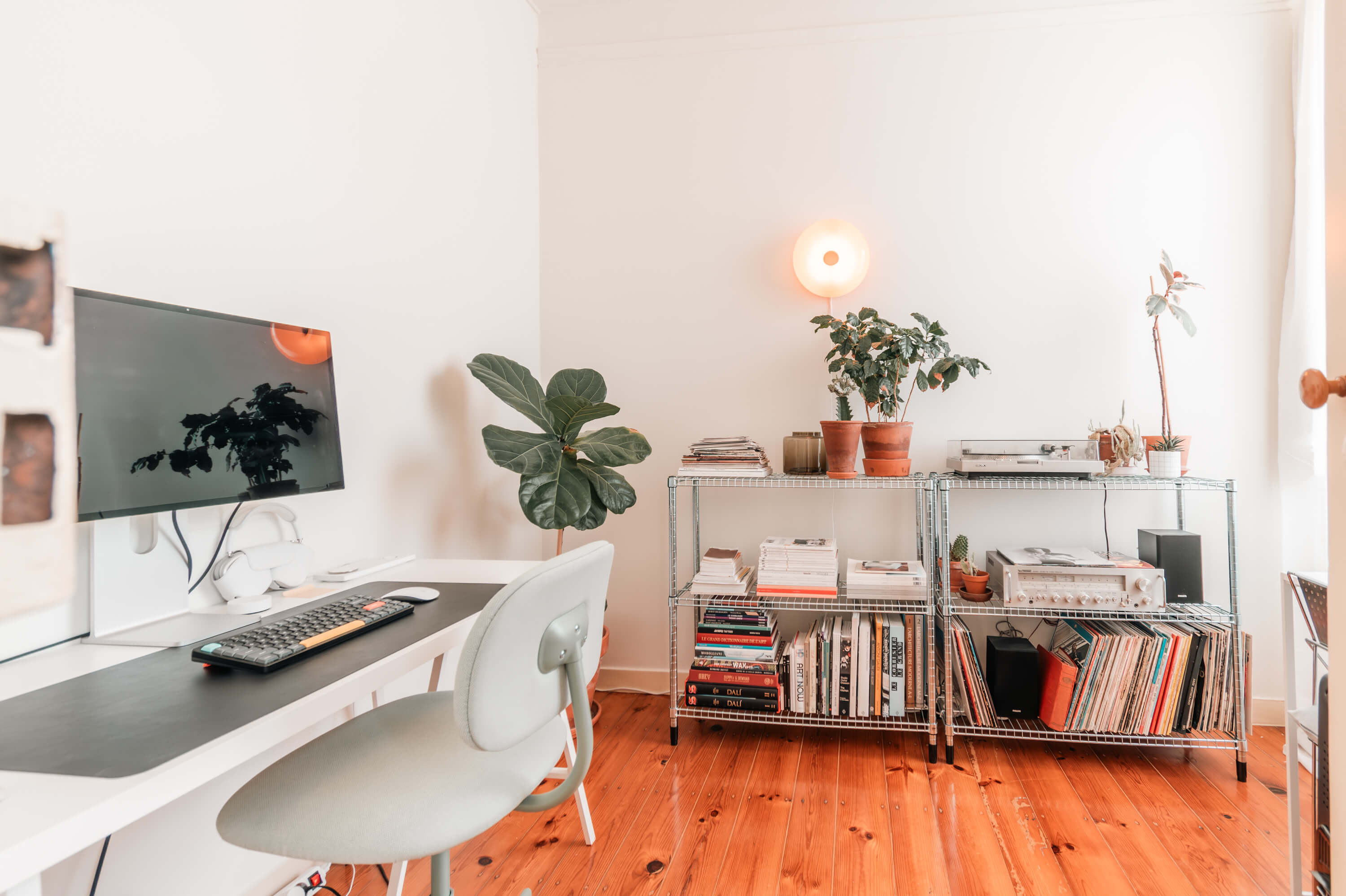 Modern home office with white desk, mounted monitor, and industrial-style metal shelving